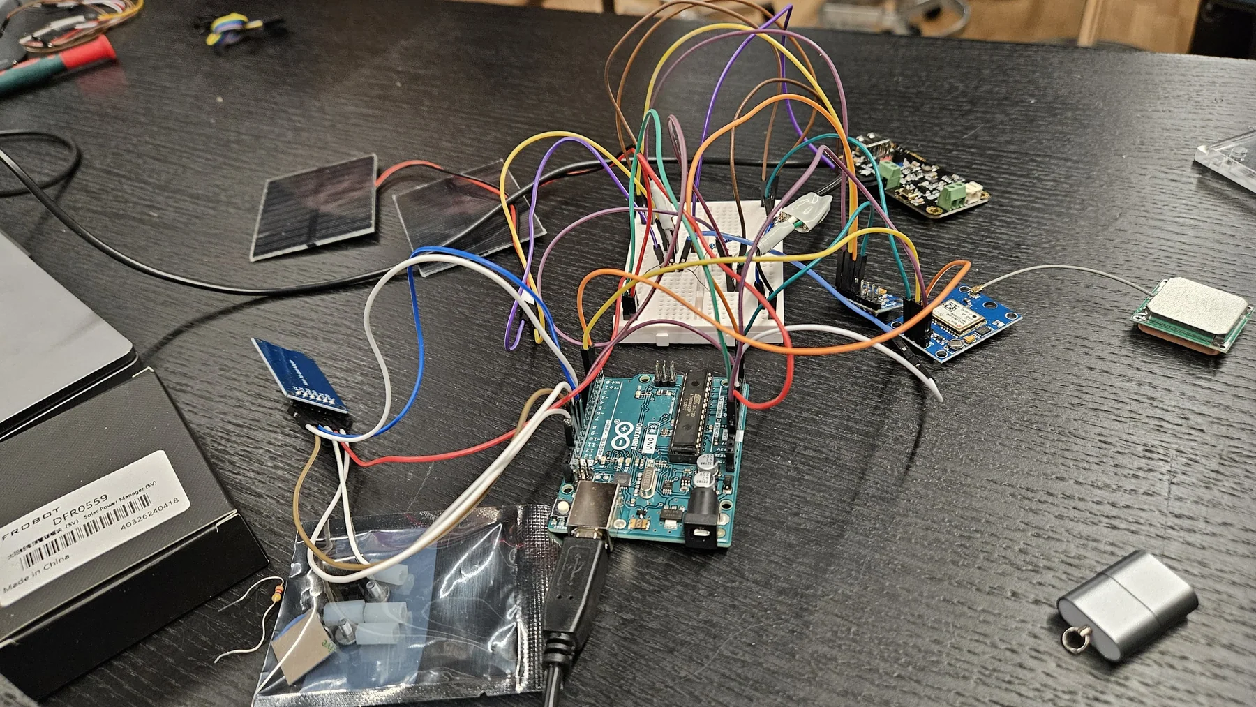 Arduino Uno, breadboard wiring, electronics modules, and a small solar panel on a workbench.